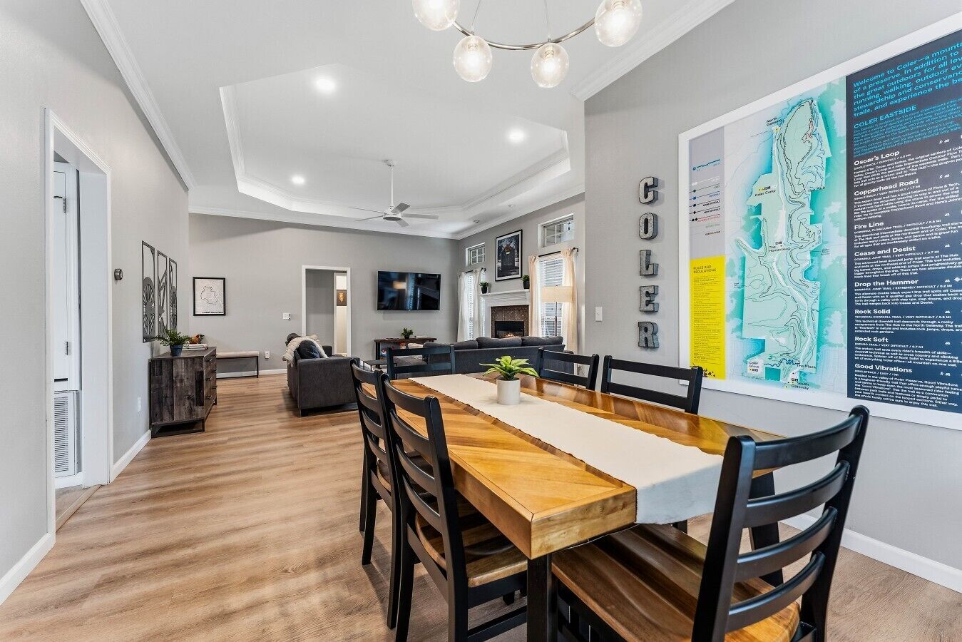 Un espace repas moderne avec une table et des chaises en bois, un ventilateur de plafond et une carte accrochée au mur.