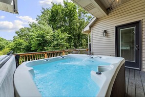Ein Whirlpool auf einer Holzterrasse mit Blick auf Bäume und ein Haus im Hintergrund.
