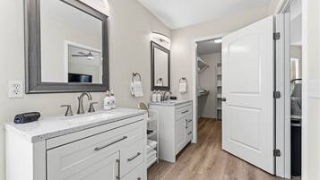 Un baño moderno con tocador doble, un espejo grande y un vestidor con puerta.