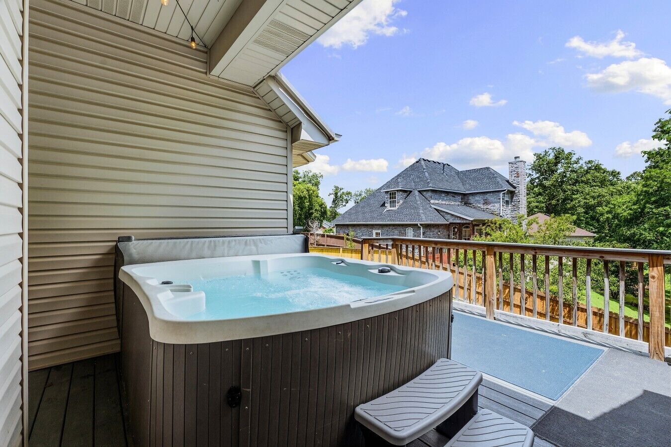 Un bain à remous sur une terrasse en bois, avec une maison visible au loin.