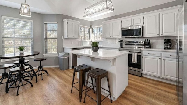 A modern kitchen with white cabinetry, a central island, stainless steel appliances, and a dining area with stools.
