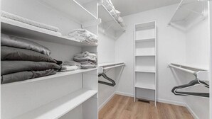 A walk-in closet with shelves for folded clothes, a hanging rod, and a vertical storage unit.