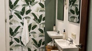 Et badeværelse med tapet med bladmotiver, to håndvaske, et spejl og en håndklædestang.