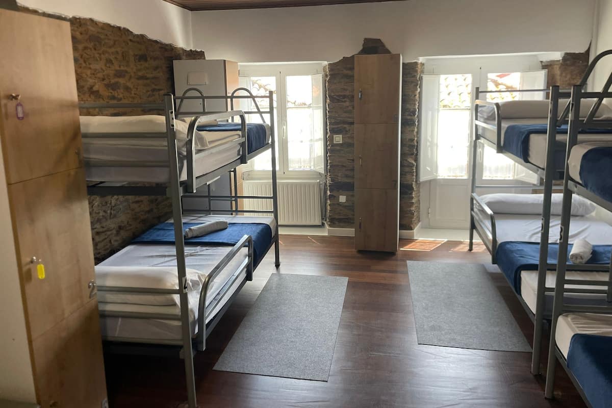 A dormitory room with bunk beds, a stone wall, a wooden door, and a radiator.