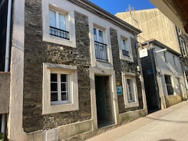 Edificio de dos pisos con fachada de piedra, varias ventanas y una puerta visible.