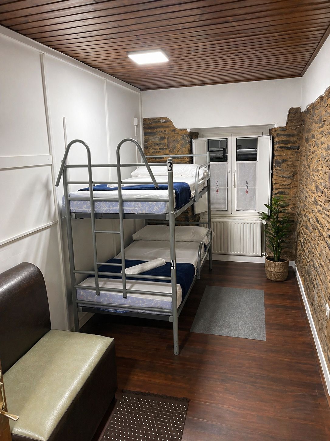 A bunk room with three bunk beds, a small seating area, a radiator, and a stone wall.