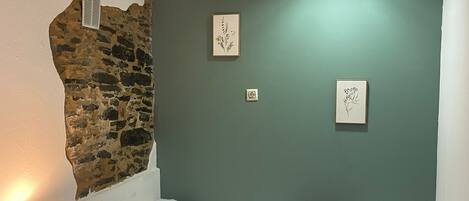 A single bed with a blue blanket, a bedside lamp, and two framed botanical prints on the wall.