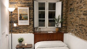 Una stanza accogliente e intima, con una parete in pietra, un letto con biancheria bianca, un comodino con una lampada e un quadro appeso al muro.