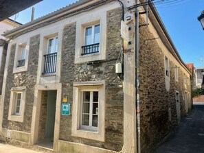 A stone building with multiple windows, a balcony, and a sign indicating a restaurant. - Albergue Amodiño (Arzua)