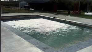 A swimming pool with a clear water surface, surrounded by a paved deck.