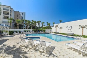 Una piscina con sillas de descanso, palmeras y un edificio al fondo.