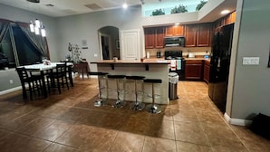 A modern kitchen with a central island, bar stools, and a dining area with a table and chairs. - Lovely 3BR ranch home in Maricopa resort community w/ pools, courts, fitness ctr (Maricopa)