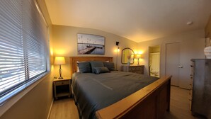 Une chambre à coucher comprenant un lit, des lampes de chevet, une table de chevet, une commode, un miroir et une fenêtre avec des stores.