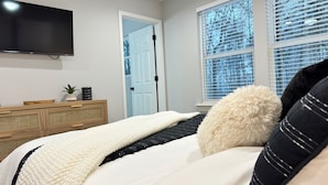 A bedroom with a bed, a dresser, a television, and a window with blinds. - Modern new townhouse near Stone Mountain. Sleeps 10. (Snellville)
