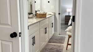 A hallway leading to a bathroom with a vanity, a mirror, and a light fixture. - Modern new townhouse near Stone Mountain. Sleeps 10. (Snellville)