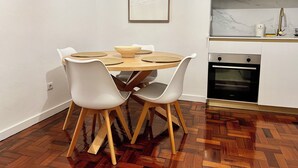 Un comedor con una mesa redonda, sillas blancas y suelo de madera.