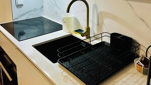 Una cocina con encimera blanca, un lavamanos negro, un grifo de acero inoxidable y un escurreplatos negro.