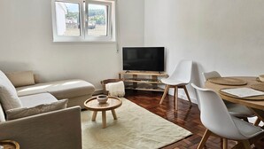 Un salón con sofá, televisor, mesa de comedor, sillas y una pequeña mesa redonda con un cuenco.