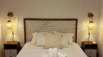 A neatly made bed with a headboard featuring a wavy design, flanked by two bedside tables with lamps, and a pair of towels on the bed.