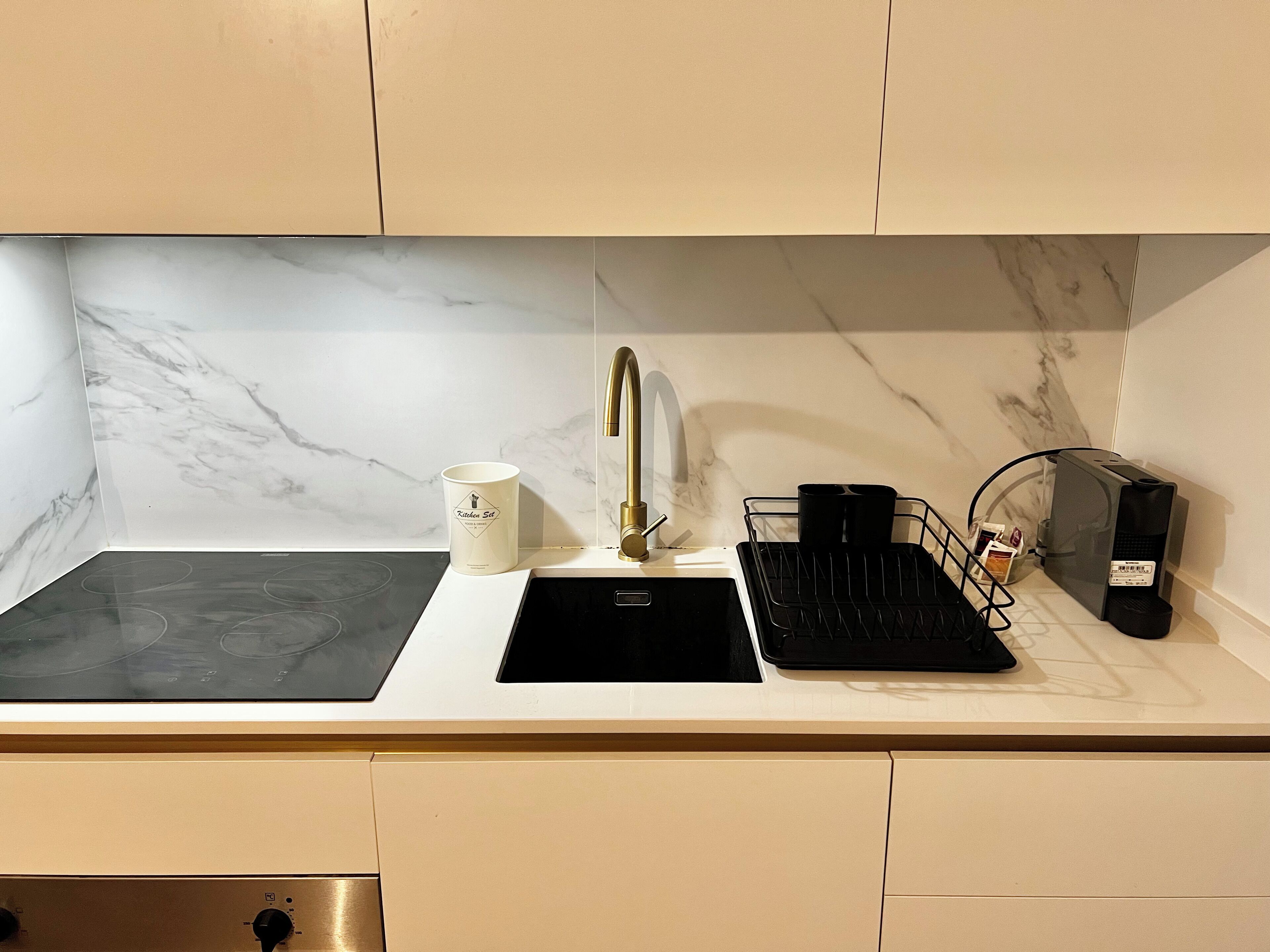 A kitchen with a black stovetop, a white sink with a gold faucet, and a coffee machine.