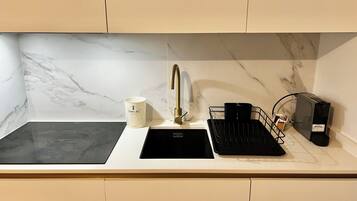 A kitchen with a black stovetop, a white sink with a gold faucet, and a coffee machine.
