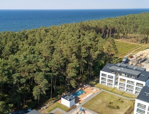 Ein Wohngebiet mit einem modernen Gebäude, einem Schwimmbad und einem dichten Wald im Hintergrund.