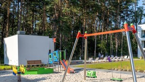 A playground with swings and slides, a small building, and a seating area with sun loungers. - Apartment Close to the Beach, With Pool (Dziwnów)