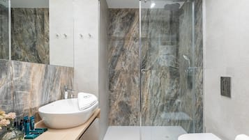 A modern bathroom with a glass-enclosed shower, a white sink, and a toilet.