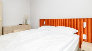 A hotel room with a bed, a nightstand, a dresser, and a wall-mounted light switch. - Apartment Close to the Beach, With Pool (Dziwnów)