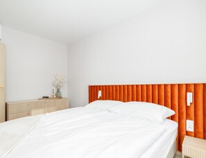 A hotel room with a bed, a nightstand, a dresser, and a wall-mounted light switch. - Apartment Close to the Beach, With Pool (Dziwnów)
