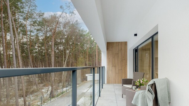 A balcony with a view of a forest, a wicker chair, and a wooden door. - Apartment Close to the Beach, With Pool (Dziwnów)