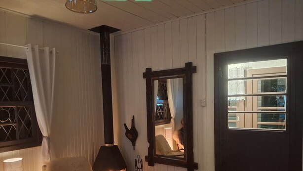 A cozy room with a fireplace, a mirror, a door, and a window with curtains. - Cozy house in the mountains (Centro Canela)