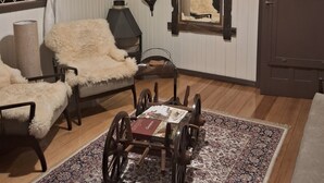 A room with a wooden floor, a large mirror, a rustic wooden cart, a fluffy chair, and a window with curtains. - Cozy house in the mountains (Centro Canela)