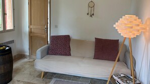 Una habitación con un sofá color beige, una puerta de madera, un atrapasueños y una lámpara con diseño geométrico.
