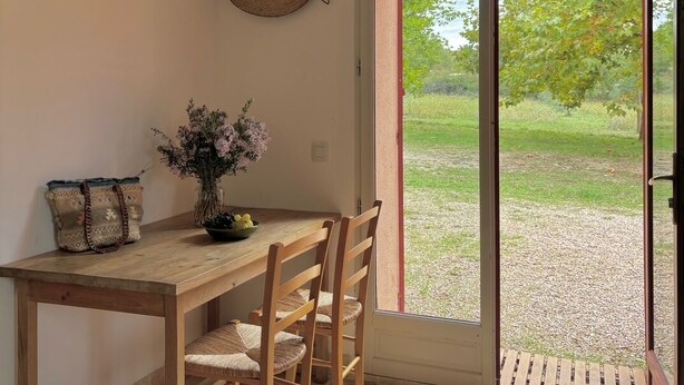 Una mesa de madera con sillas, una cesta tejida y un florero con flores.