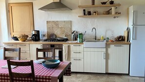 Una cocina con armarios blancos, una estufa, un fregadero y una zona de comedor con mantel a cuadros.
