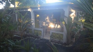 Un edificio moderno con un patio cubierto rodeado de plantas tropicales y un sendero de grava.