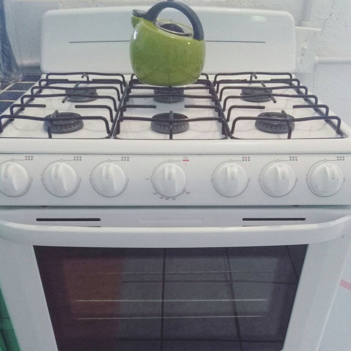 A white stove with six burners and a green kettle on top.