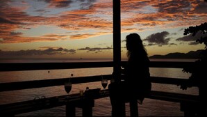 Silueta de una persona sentada a una mesa con vista al atardecer sobre el océano.