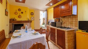 A dining area with a table set for four, a kitchen with wooden cabinets, a gas stove, and a television. - 2 bedroom lovely home in Frontale (Frontale)