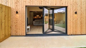 A modern building with a wooden exterior and a glass door leading to an interior space with a sofa and a dining area.