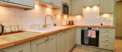 A kitchen with light green cabinets, a stainless steel sink, a microwave, and a built-in oven.