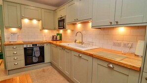 Una cucina moderna con mobili chiari, un piano di lavoro in legno, forno a incasso, microonde e lavello con scolapiatti.