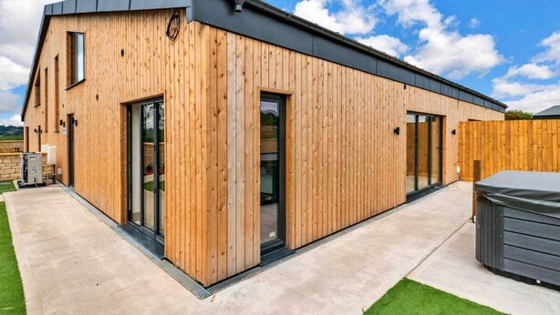 Un edificio moderno in legno con ampie porte e finestre in vetro, un patio in cemento e una recinzione in legno.