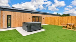 Un edificio moderno con rivestimento in legno, una vasca idromassaggio coperta e un tavolo da picnic in un prato curato.