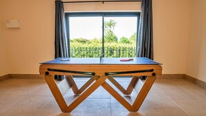 A ping pong table in a room with a large window, curtains, and a view of greenery outside. - Little Rissington - Barn Six (Little Rissington)