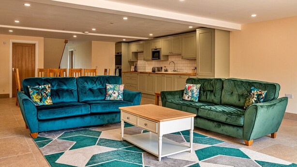 A living room with two sofas, a coffee table, and a kitchen in the background. - Little Rissington - Barn Six (Little Rissington)