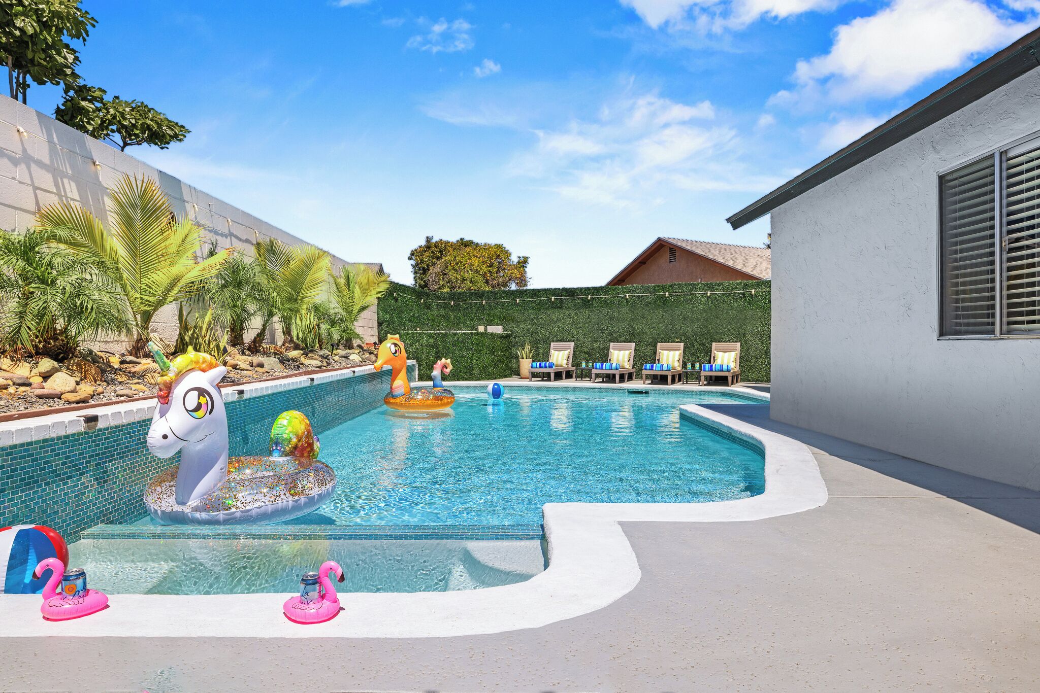 Una piscina con gonfiabili a forma di unicorno, sedie a sdraio e una zona verde con palme.