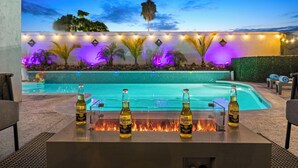 Zona de piscina al aire libre con un elemento decorativo de fuego y tres botellas de cerveza Corona Extra.