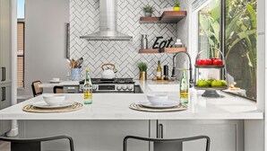 Una cocina moderna con una isla central, salpicadero blanco con patrón de espiga y una ventana con vistas a la vegetación.